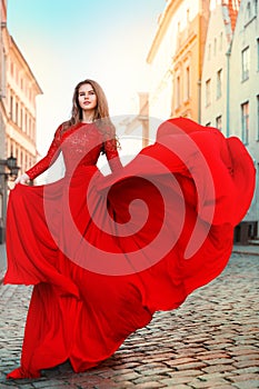 Beautiful Woman in Waving Long Fluttering Red Dress Walking on the City Street. Outdoor Brunette Portrait in Sun
