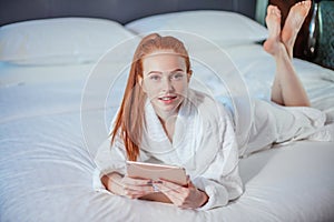 Beautiful woman wearing bathrobe and using digital tablet while relaxing on bed