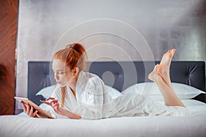 Beautiful woman wearing bathrobe and using digital tablet while relaxing on bed