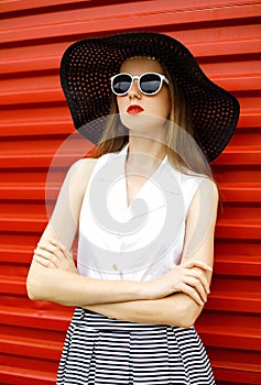 Beautiful woman wearing a black straw hat, sunglasses and striped skirt over red