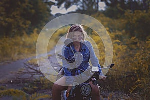 beautiful woman wearing blue jeans jacket sitting on enduro motorcycle against colorful natural background