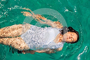 Beautiful woman wearing blue white swimsuit relaxing in the sea enjoying summer in Zakynthos island in Greece.