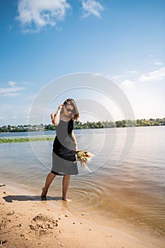 Beautiful woman wearing coctail black dress standing on water lake