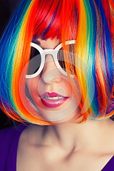 beautiful woman wearing colorful wig and white sunglasses against wooden background