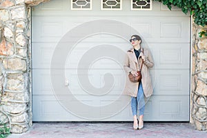 Beautiful woman wearing jeans and trench, standing against wall on city street. Casual fashion, elegant everyday look