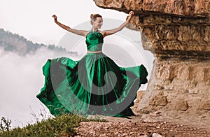 Beautiful woman wearing long green dress dancing on the edge of a cliff. Mezmay.