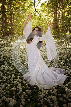 Beautiful woman wearing a long white dress dancing in a forest