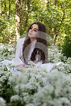 Beautiful woman wearing a long white dress sitting in a forest