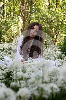 Beautiful woman wearing a long white dress sitting in a forest o