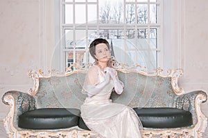 Beautiful woman wearing medieval vintage Edwardian Style dress sitting on the sofa