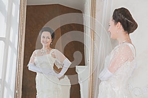 Beautiful woman wearing medieval vintage Edwardian Style dress stand near mirror