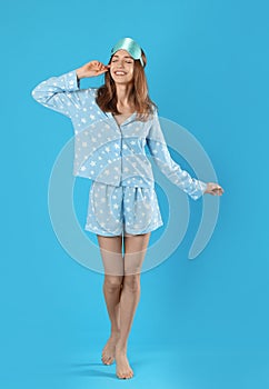 Beautiful woman wearing pajamas and sleep mask on blue background. Bedtime