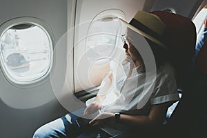 Beautiful woman wearing a straw hat using a smart phone While sitting on the plane To travel and relax Travel ideas Working while