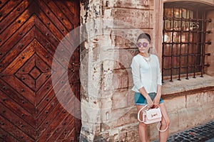 Beautiful woman wearing stylish outfit with accessories outdoors. Girl walking along old city street