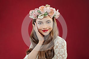 Beautiful woman wearing summer rose wreath portrait. Smiling model with flowers on red background