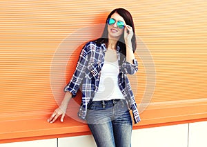 Beautiful woman wearing a sunglasses and checkered shirt over colorful orange