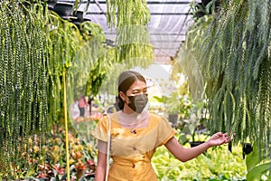 Beautiful woman wearing surgical face mask and buying plants at garden center