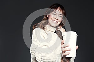 Beautiful woman wearing sweater shows paper disposable coffee cup. Drinking coffee, smiling and laughing.