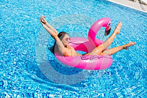 Beautiful woman, wearing swimsuit, lying on a pink flamingo air mattress in a pool of blue water, summer