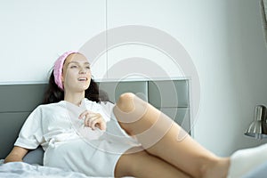 A beautiful woman wearing a towel and a white bathrobe and pink headband with happy and relaxing on the bed at a condominium in