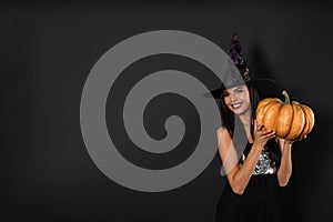 Beautiful woman wearing witch costume with pumpkin for Halloween party on black background