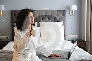 Beautiful woman in a white bathrobe with a cup of coffee on the bed at the hotel.