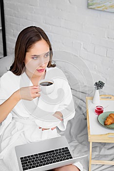 beautiful woman in white bathrobe with laptop drinking coffee