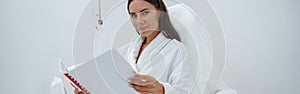 Beautiful woman in white bathrobe reading magazine while sitting in luxury wellness spa centre