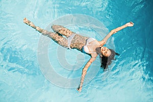 Beautiful woman in white bikini floating in swimming pool