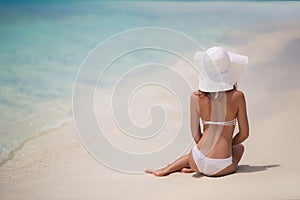 Beautiful woman in a white bikini and hat on the beach.