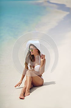 Beautiful woman in a white bikini and hat on the beach.
