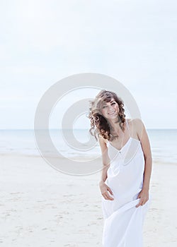 Beautiful woman in a white dress on the ocean coast. Happy girl on the beach, the wind fluttering hair.