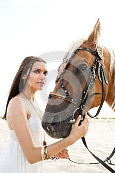 Beautiful woman in white dress posing with horse against desert