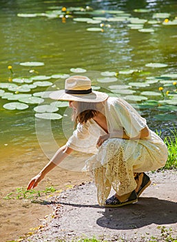 Beautiful woman in a white dress and straw hat on the shore of an old pond