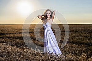 Beautiful woman in a white dress in a wheat field at sunset