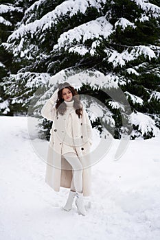 Beautiful woman in white fur posing near spruces in snow. Winter