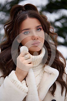 Beautiful woman in white fur posing near spruces in snow. Winter