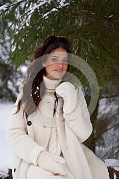 Beautiful woman in white fur posing near spruces in snow. Winter