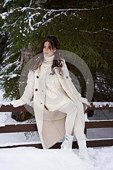 Beautiful woman in white fur posing near spruces in snow. Winter