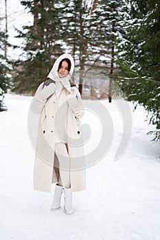Beautiful woman in white fur posing near spruces in snow. Winter
