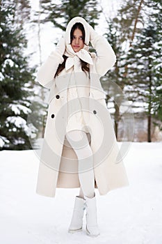 Beautiful woman in white fur posing near spruces in snow. Winter