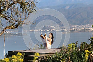 A beautiful woman in a white gymnastic jumpsuit performs yoga on the background of the mountains and the sea