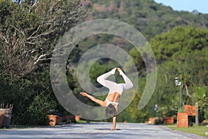 A beautiful woman in a white gymnastic jumpsuit is engaged in yoga.