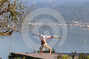 A beautiful woman in a white gymnastic jumpsuit is engaged in yoga on the background of the mountains and the sea