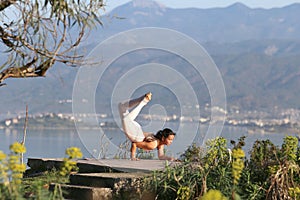A beautiful woman in a white gymnastic jumpsuit is engaged in yoga on the background of the mountains and the sea