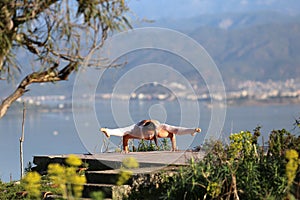 A beautiful woman in a white gymnastic jumpsuit performs yoga on the background of the mountains and the sea