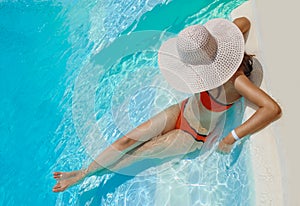 Beautiful woman in white hat rests near the pool