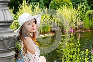 Beautiful woman in white hat sitting near the lake