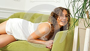 Beautiful woman in white lingerie sitting on green sofa at home - happy morning