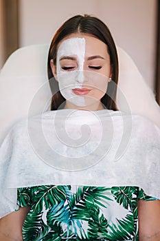 Beautiful woman with white mask on hulf of face. Attractive brunrtte woman in beauty salon